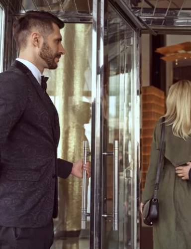 Doorman öffnet Tür eines Geschäfts für Frau und Mann
